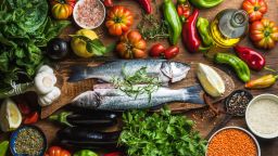Raw uncooked seabass fish with vegetables, grains, herbs and spices on chopping board over rustic wooden background, top view; Shutterstock ID 415721434